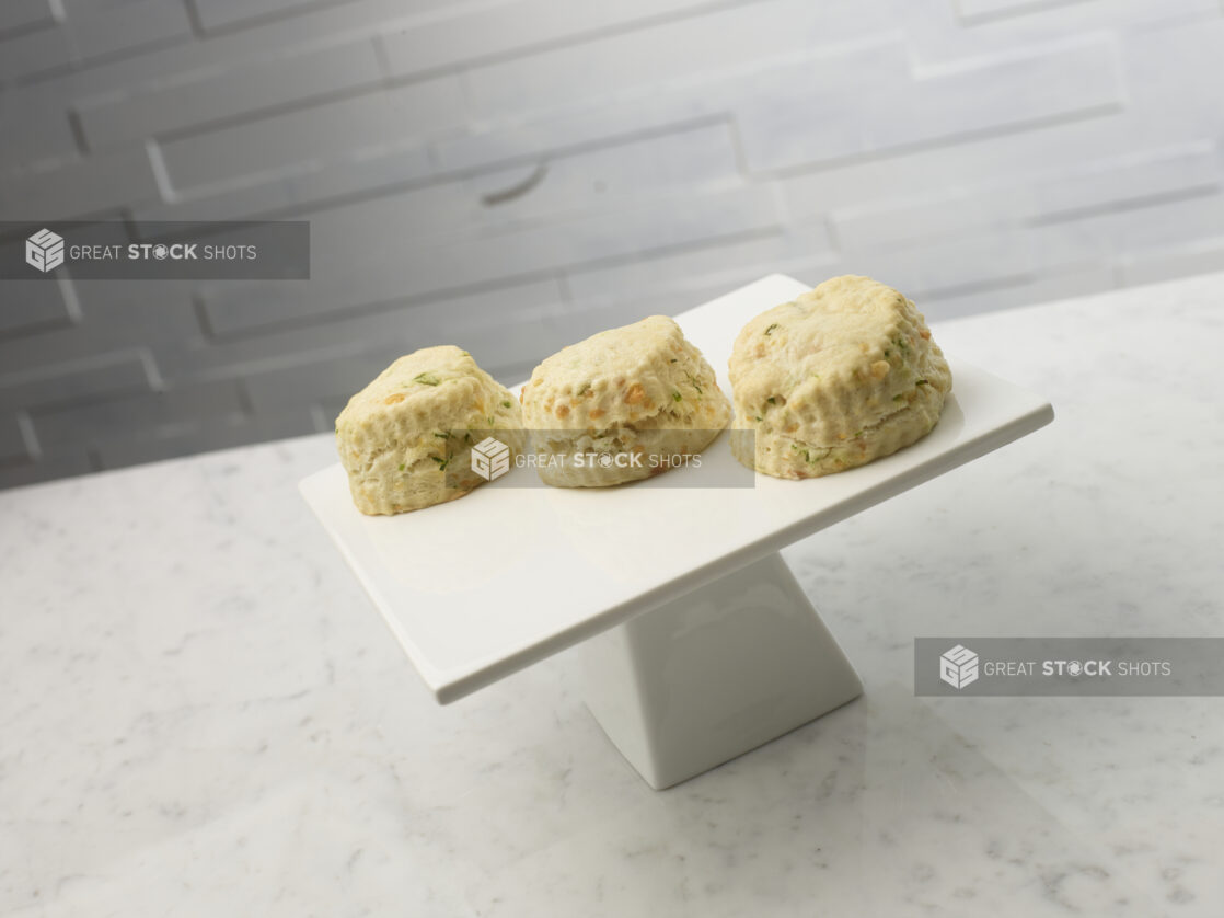 Savory cheese and chive tea biscuits on a white ceramic cake stand on a white marble background