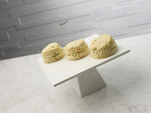 Savory cheese and chive tea biscuits on a white ceramic cake stand on a white marble background