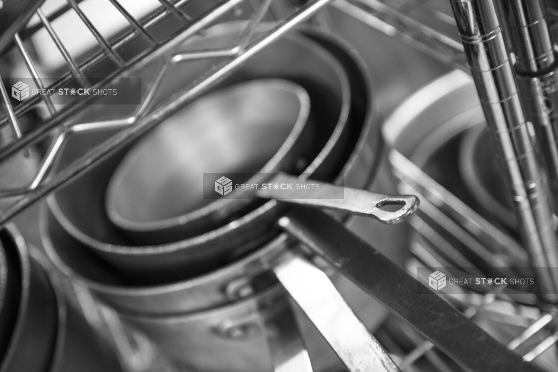 Black and white photo of sauté pans on a metal rack, close up view