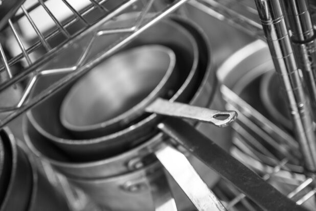 Black and white photo of sauté pans on a metal rack, close up view