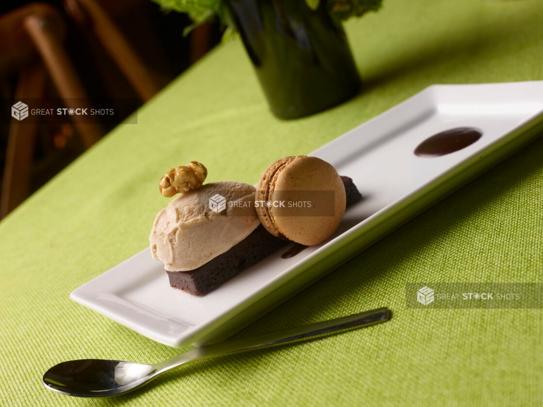 Mocha macaron, chocolate cake and hazelnut gelato elegantly displayed on a white rectangular plate on a lime green tablecloth