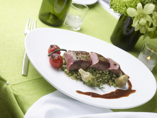 Grilled pork tenderloin over quinoa salad with grilled cherry tomato and artichoke hearts on a lime green tablecloth, elegant setting