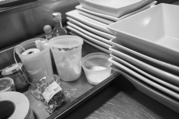 Black and white photo of a restaurant kitchen prep area with white square bowls and cooking accessories