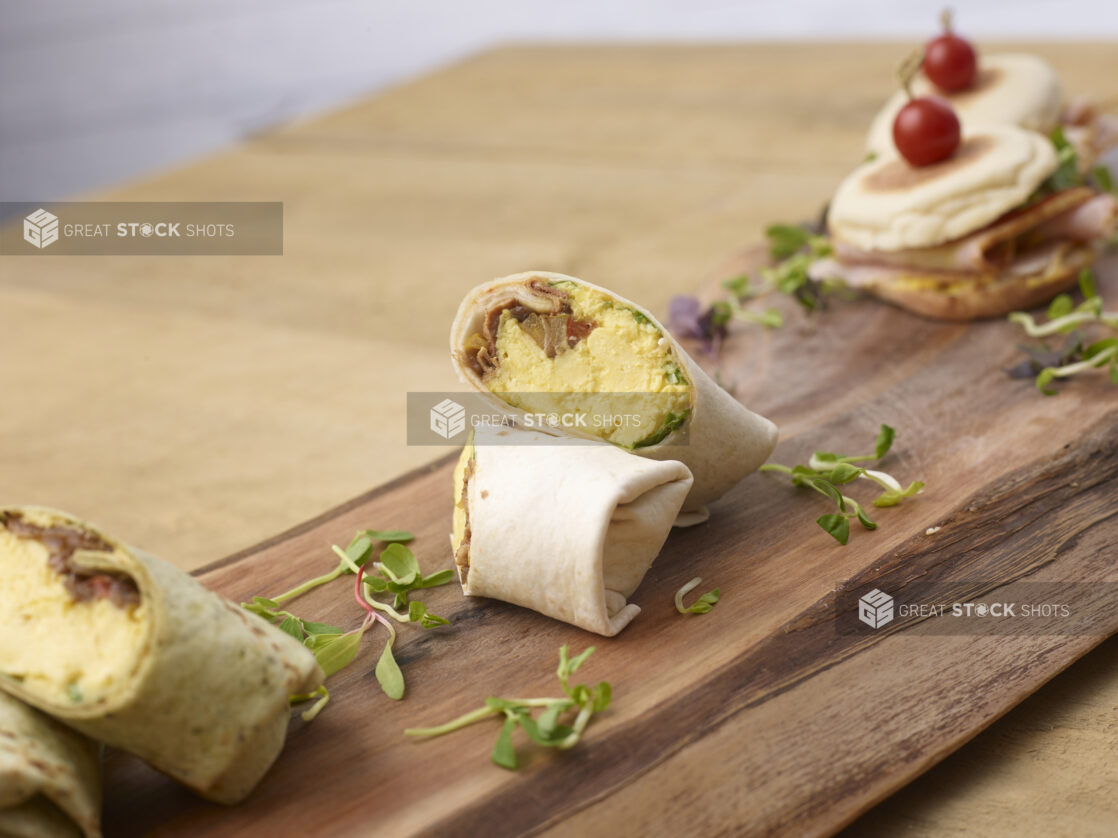 Breakfast wraps and sandwich on a wood serving board with micro greens garnish