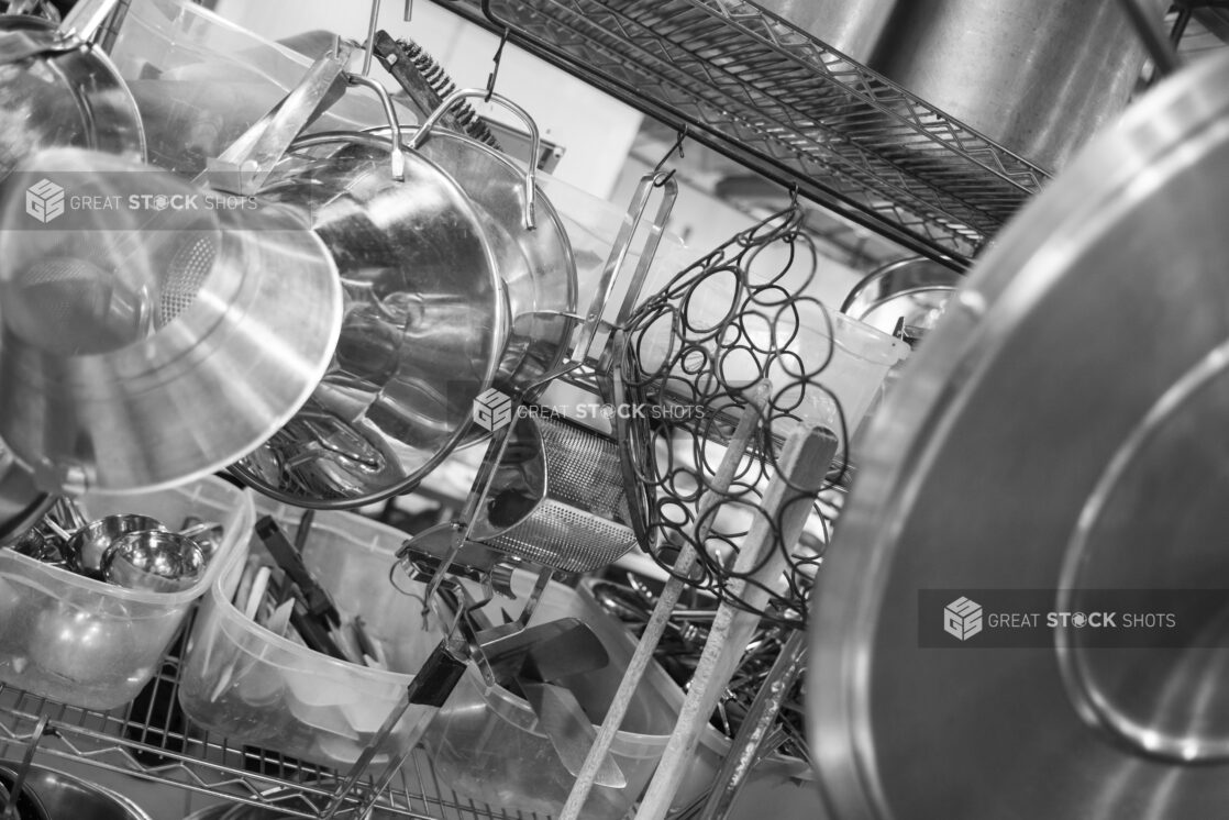 Black and white photo of various restaurant kitchen equipment on a metal wire rack