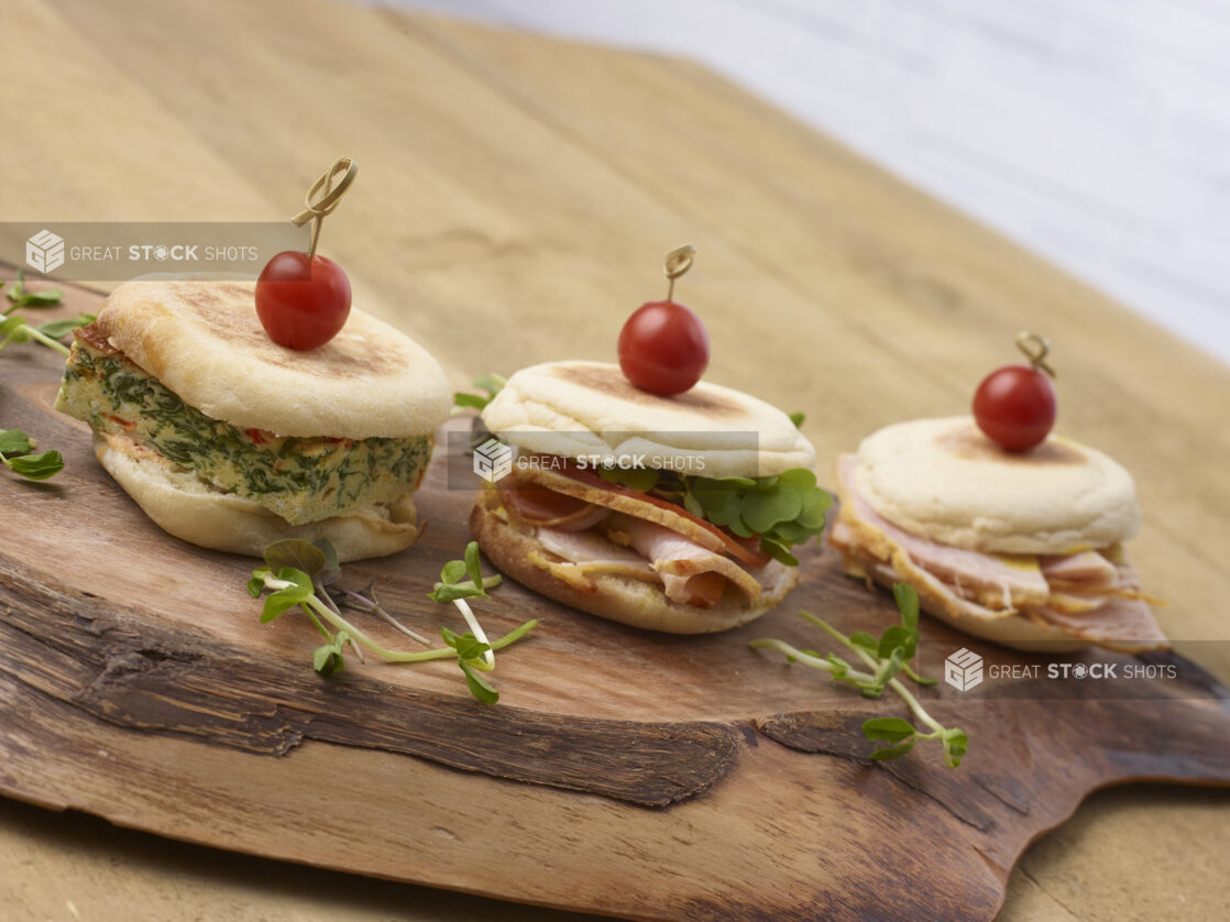 3 breakfast sandwiches in a close up view on an artistic wooden board with pea shoot garnish