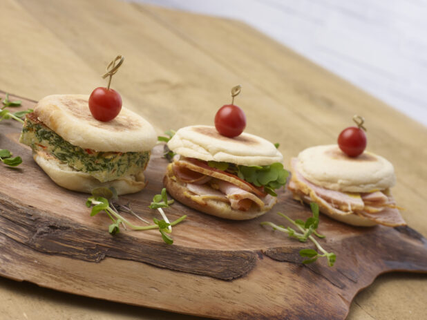 3 breakfast sandwiches in a close up view on an artistic wooden board with pea shoot garnish