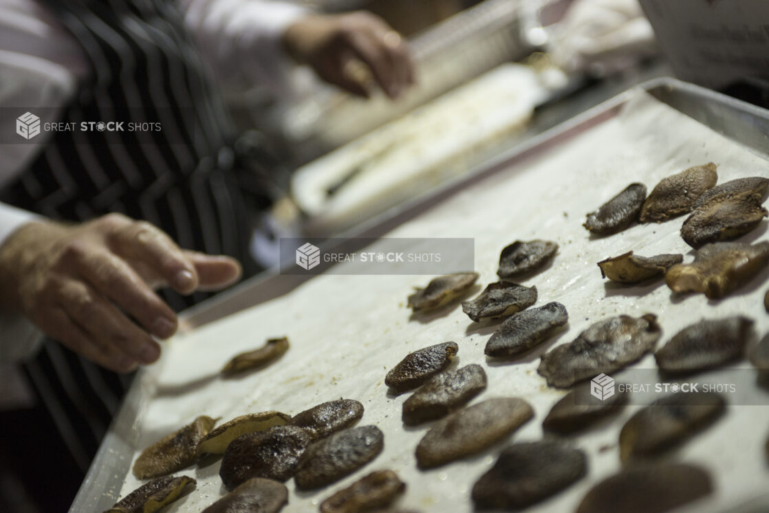 Shitake mushrooms on a baking sheet with a chef reaching for the mushrooms in a kitchen setting