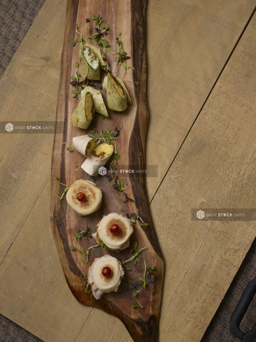 Artisanal breakfast sandwiches and wraps on an artistic wooden serving board with pea shoot garnish