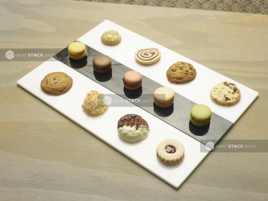 Mini dessert tray on an elegant white and black rectangular platter with macarons and cookies on a wooden background