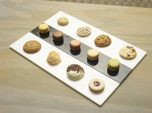 Mini dessert tray on an elegant white and black rectangular platter with macarons and cookies on a wooden background