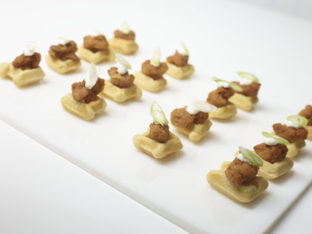 Southern fried chicken and waffle appetizer on a white rectangular board with a white background