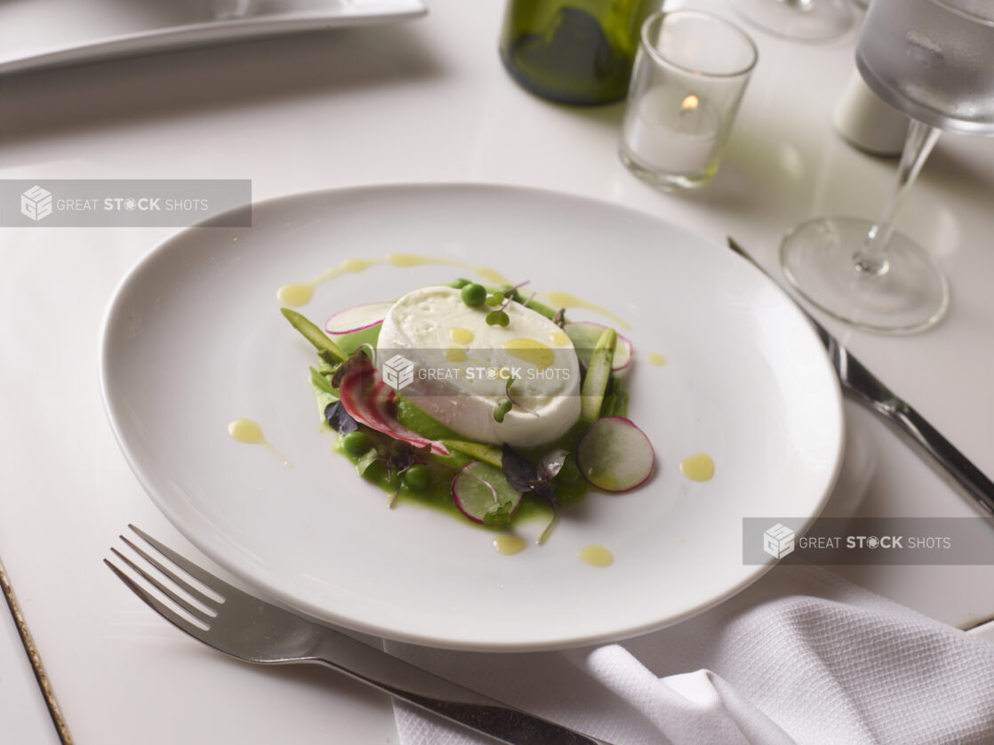 Buffalo mozzarella salad with mixed green, radish, candy-striped radish, fresh peas and an olive oil drizzle in an elegant setting