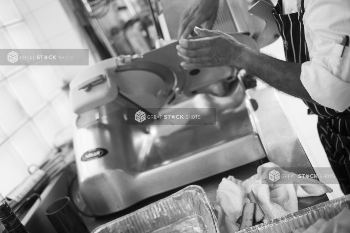 Black and white photo of chef using a meat slicer in a restaurant setting