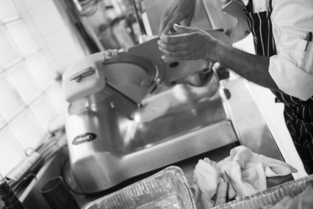 Black and white photo of chef using a meat slicer in a restaurant setting
