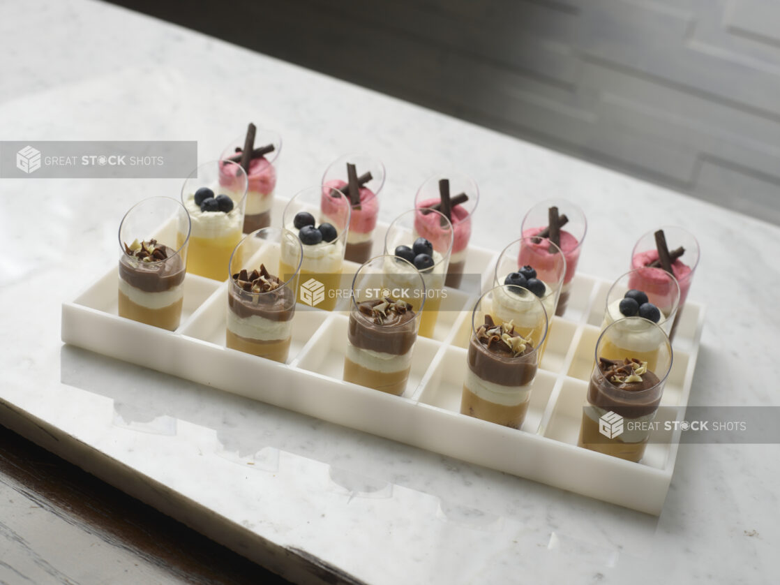 Elegant mini chocolate, mango and strawberry mousse, displayed in a white partitioned tray on a white marble background