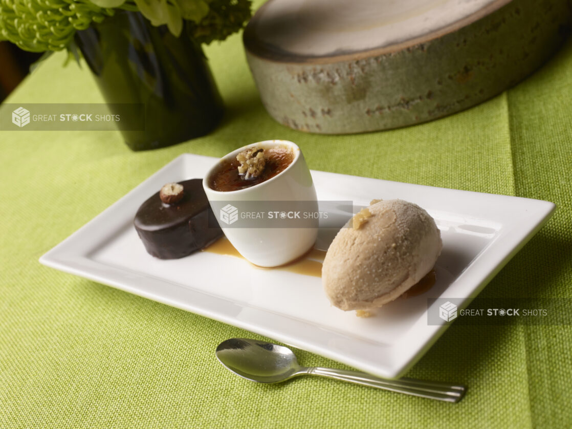 Mini Sacher torte, Creme Brulé and Hazelnut gelato on a rectangular white plate with caramel garnish on a lime green tablecloth with flowers in a vase