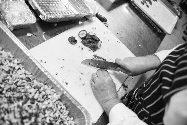 Black and white photo of a chef chopping shitake mushrooms in a prep kitchen