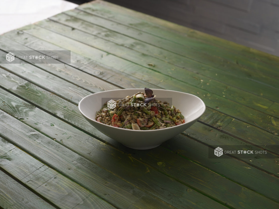 Lentil salad with red bell peppers, red onion and asparagus with a sprig of purple basil on a hunter green wooden table