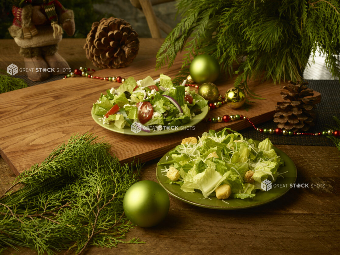 Greek salad and Caesar salad on rustic green plates on wooden background in a Christmas setting