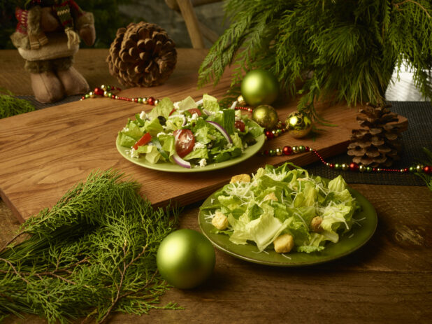 Greek salad and Caesar salad on rustic green plates on wooden background in a Christmas setting