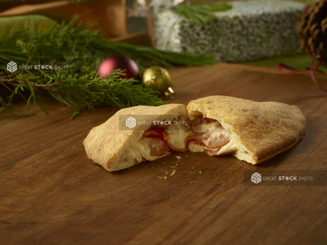 Pepperoni calzone cut in half with melted ingredients inside on a rustic wooden table in a Christmas setting