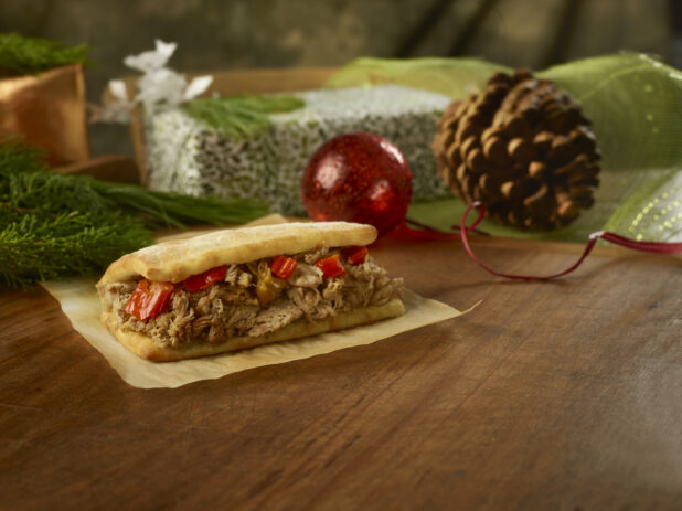 Roasted chicken flatbread sandwich with hot peppers on parchment paper on a rustic wooden table in a Christmas setting