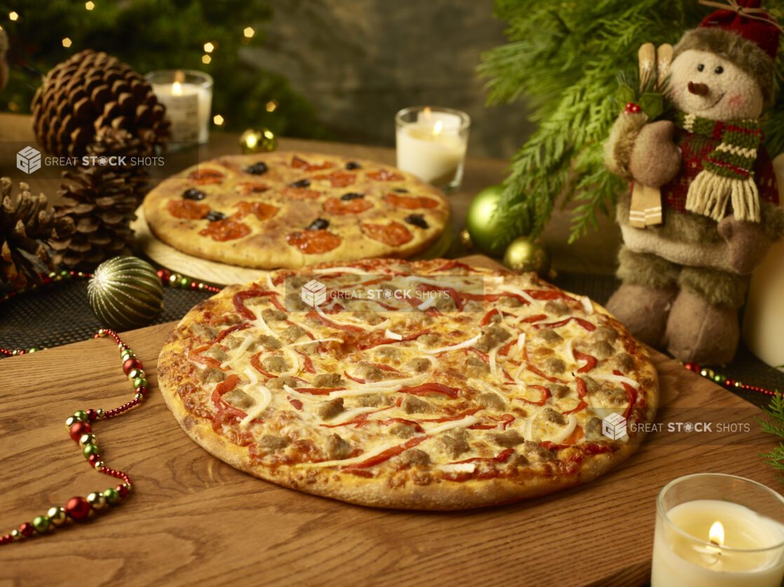 Whole pizza with sausage, onion and roasted red pepper with a whole focaccia with black olives and sundried tomatoes in the background in a christmas setting