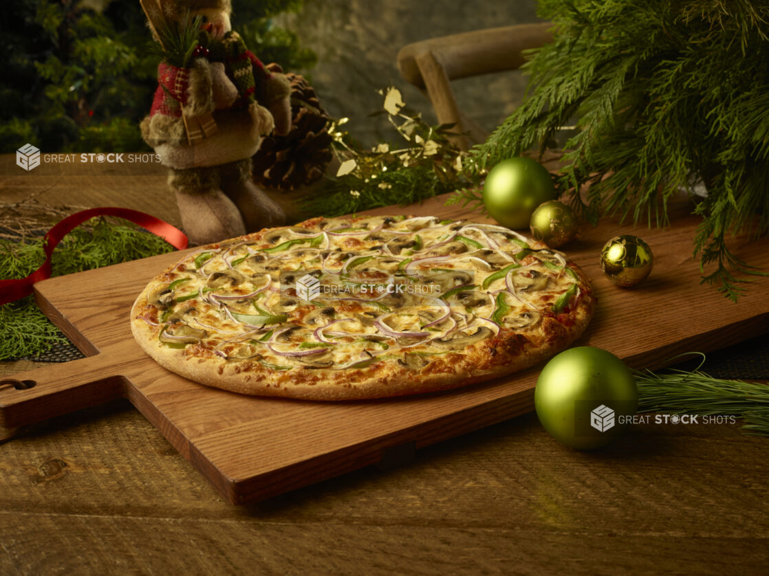 Whole vegetarian pizza with mushrooms, onions and green peppers on a wooden board in a Christmas setting