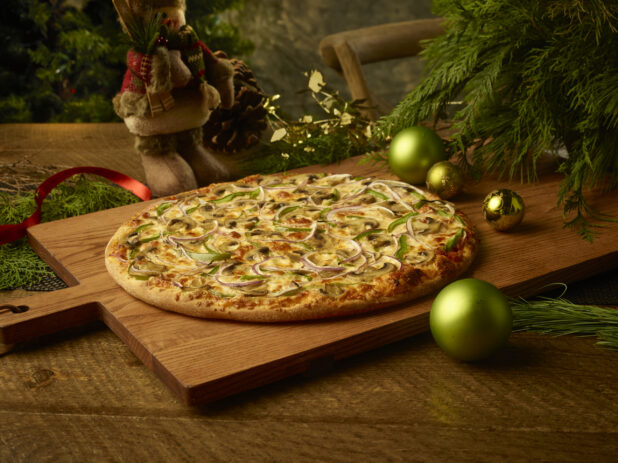 Whole vegetarian pizza with mushrooms, onions and green peppers on a wooden board in a Christmas setting