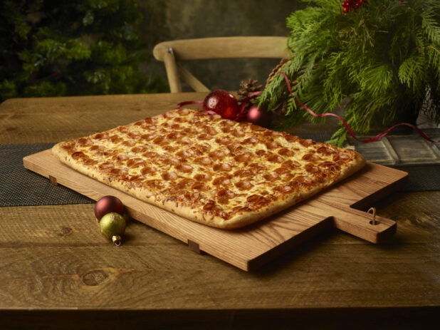 Party size pepperoni pizza on a wooden board on a rustic wooden table in a Christmas setting