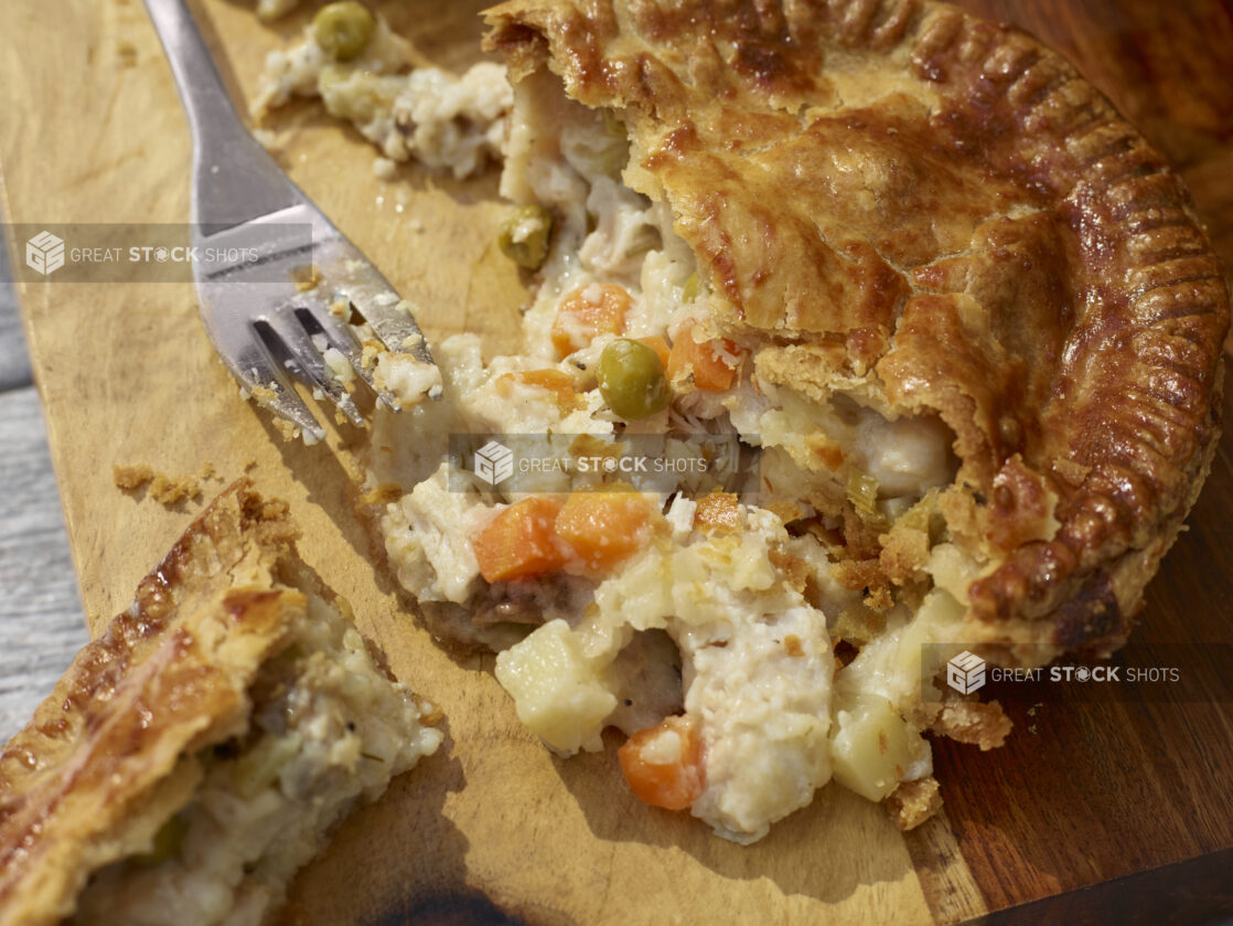 Chicken pot pie cut open on a wooden cutting board with a fork, close-up, overhead view