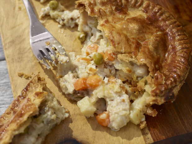 Chicken pot pie cut open on a wooden cutting board with a fork, close-up, overhead view