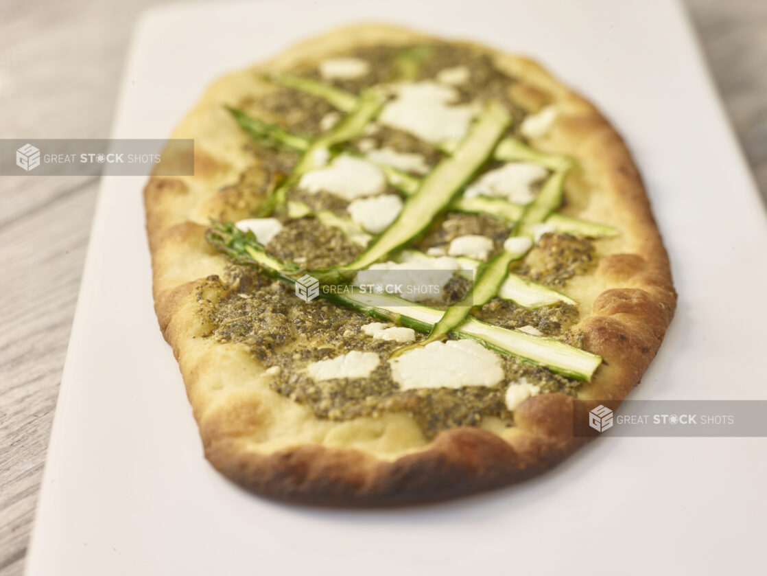 Middle Eastern zaatar flatbread with sliced asparagus and goat cheese on a white board on a grey wooden background