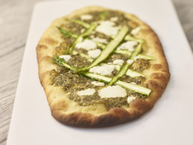 Middle Eastern zaatar flatbread with sliced asparagus and goat cheese on a white board on a grey wooden background