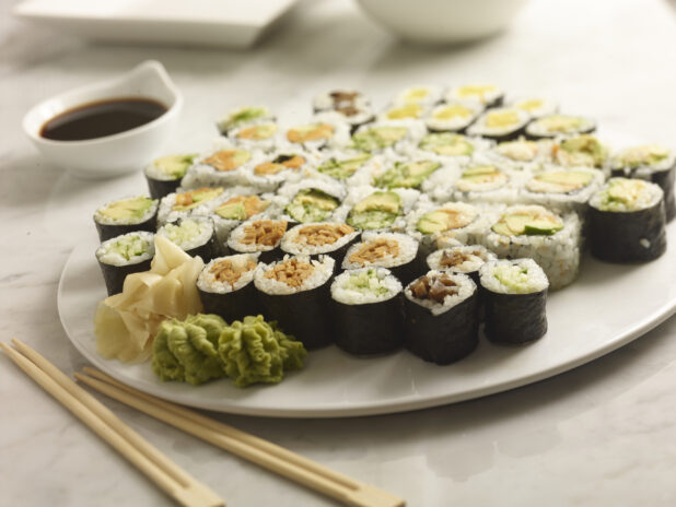 Assorted Maki sushi on a round white platter with wasabi, pickles ginger, chop sticks and soya sauce