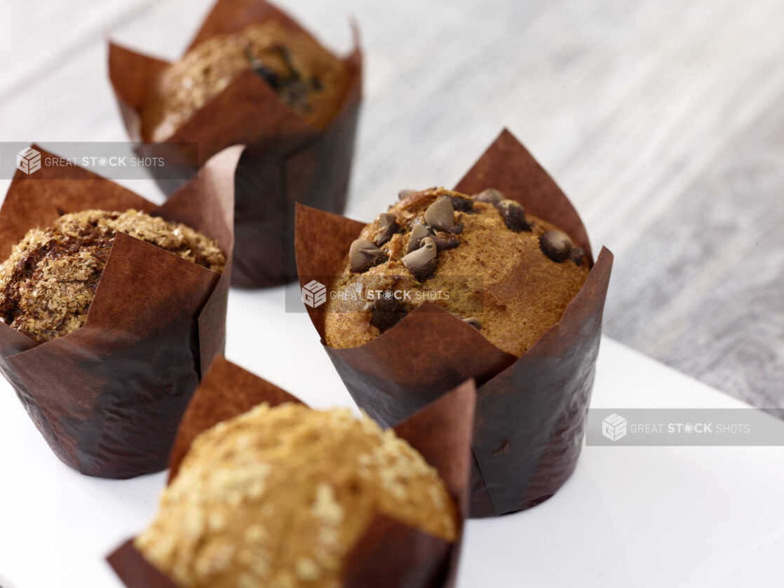 Assorted muffins in brown parchment paper on a white board on a grey wooden background