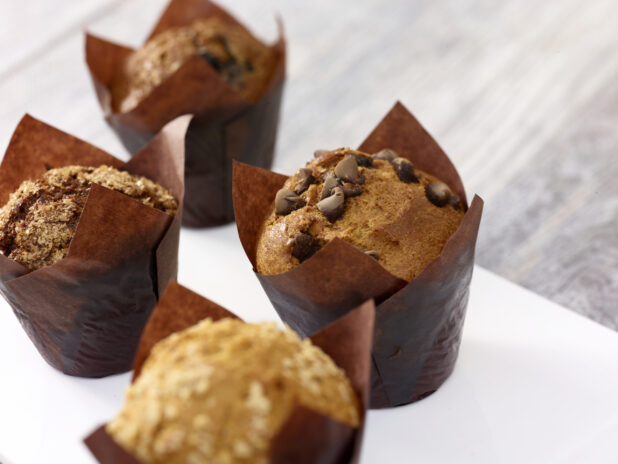 Assorted muffins in brown parchment paper on a white board on a grey wooden background