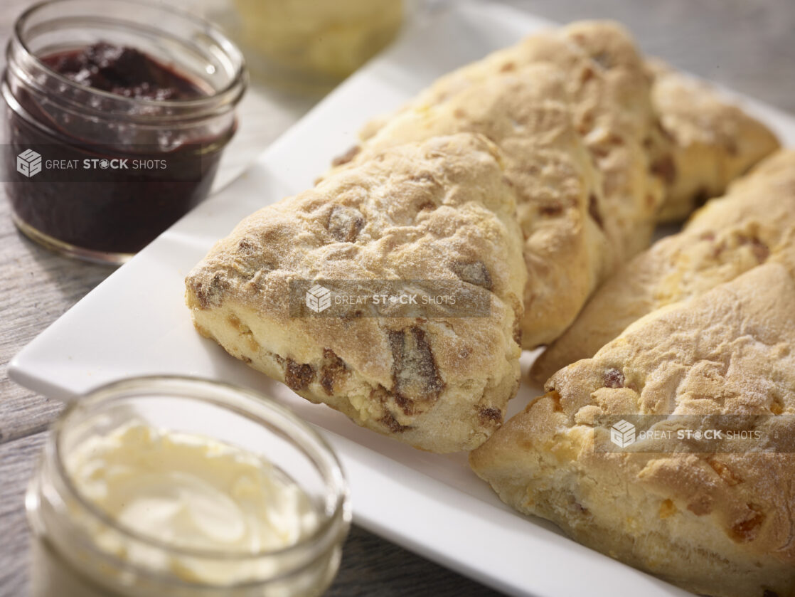 Scones/tea biscuits on a square white platter with mason jars of butter and jam, close up view