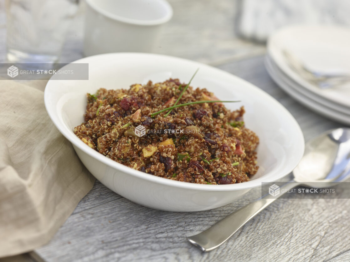 Rustic quinoa salad in a white bowl on a grey wooden background with accessories