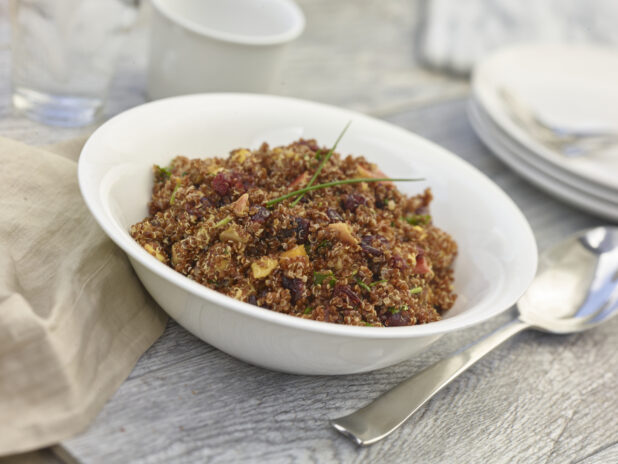 Rustic quinoa salad in a white bowl on a grey wooden background with accessories