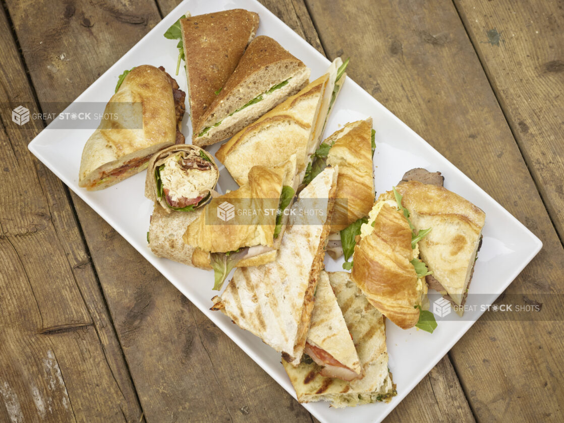 Assorted sandwich platter with sandwiches on croissants, wraps, panini, flatbread, tortilla and baguettes on a rustic wooden background