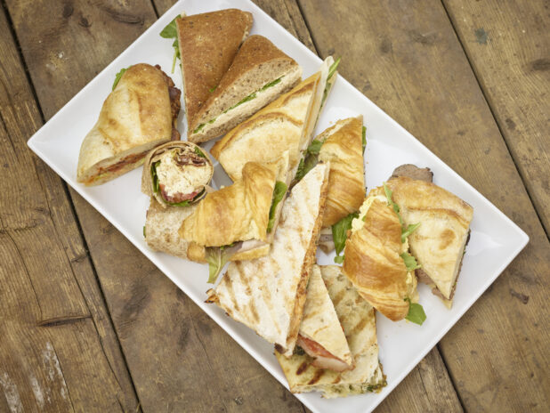 Assorted sandwich platter with sandwiches on croissants, wraps, panini, flatbread, tortilla and baguettes on a rustic wooden background