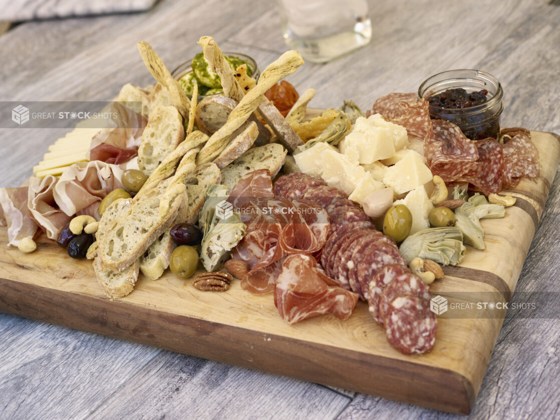 Charcuterie with various salami and prosciutto, cheeses, olives, breads and accompaniments on a wooden board