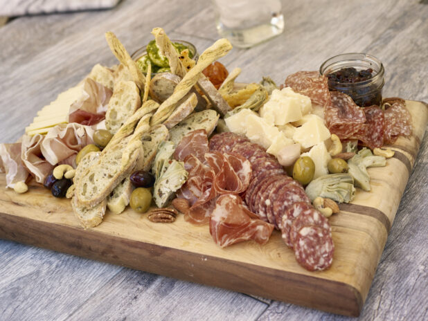 Charcuterie with various salami and prosciutto, cheeses, olives, breads and accompaniments on a wooden board