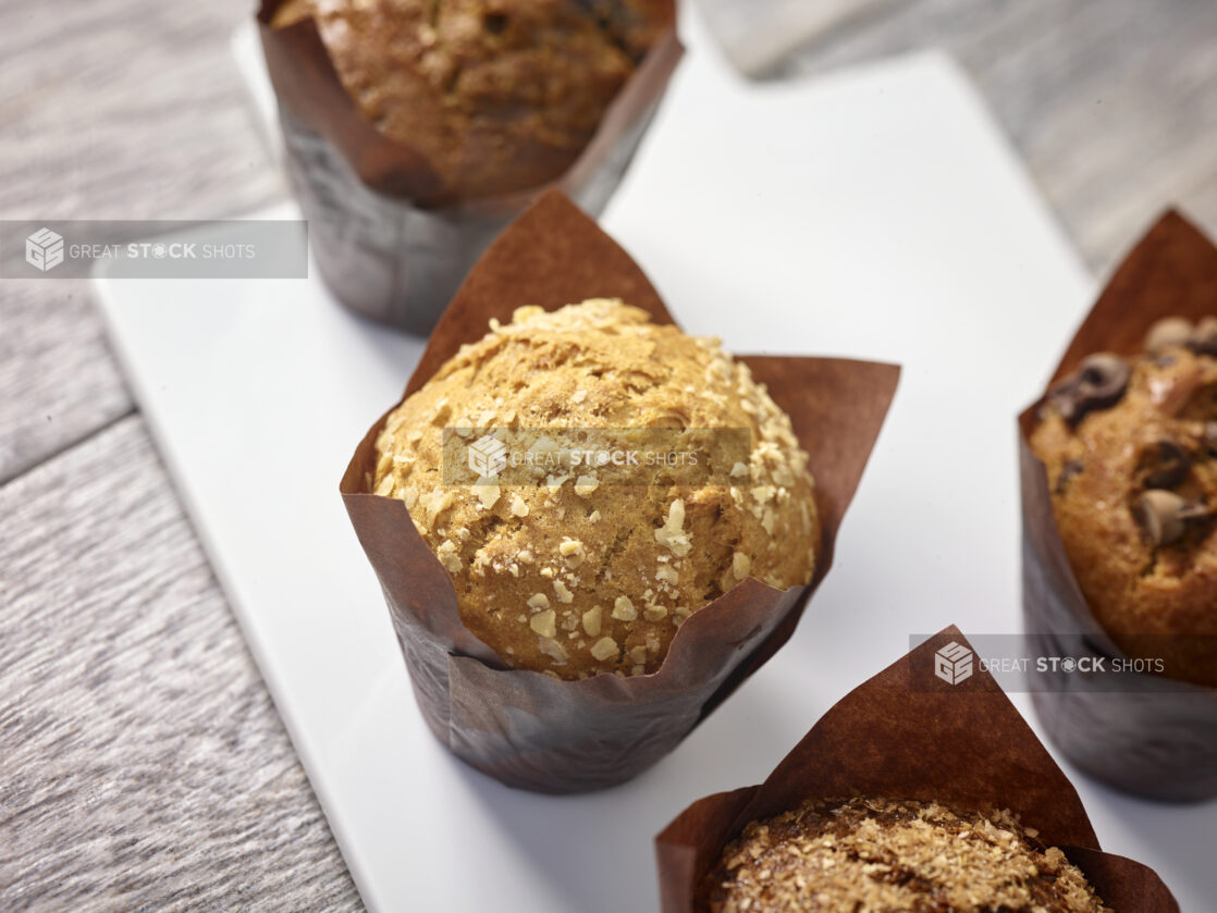 Assorted muffins wrapped in brown parchment paper on a white board on a grey wooden background