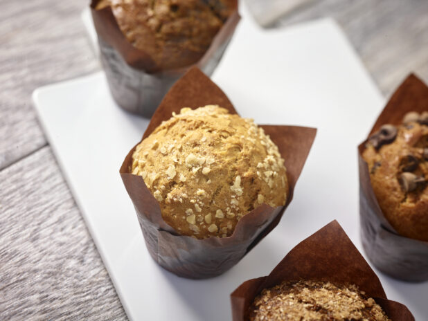 Assorted muffins wrapped in brown parchment paper on a white board on a grey wooden background