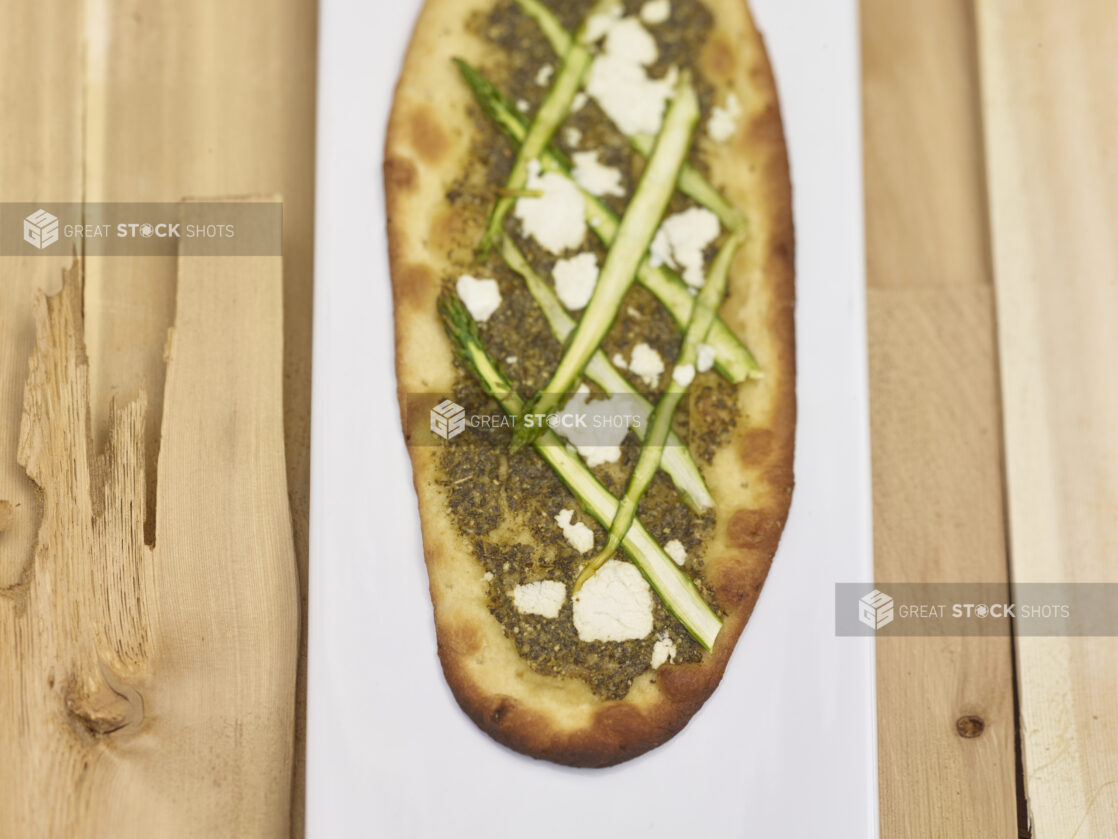 Middle Eastern Zaatar flatbread with sliced asparagus and goat cheese on a white board with a wooden background