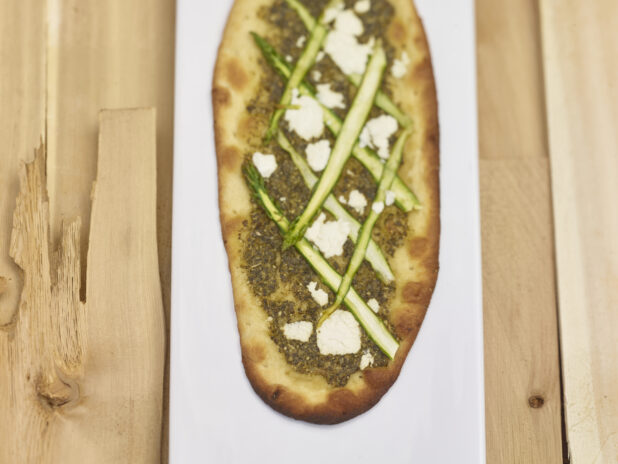 Middle Eastern Zaatar flatbread with sliced asparagus and goat cheese on a white board with a wooden background