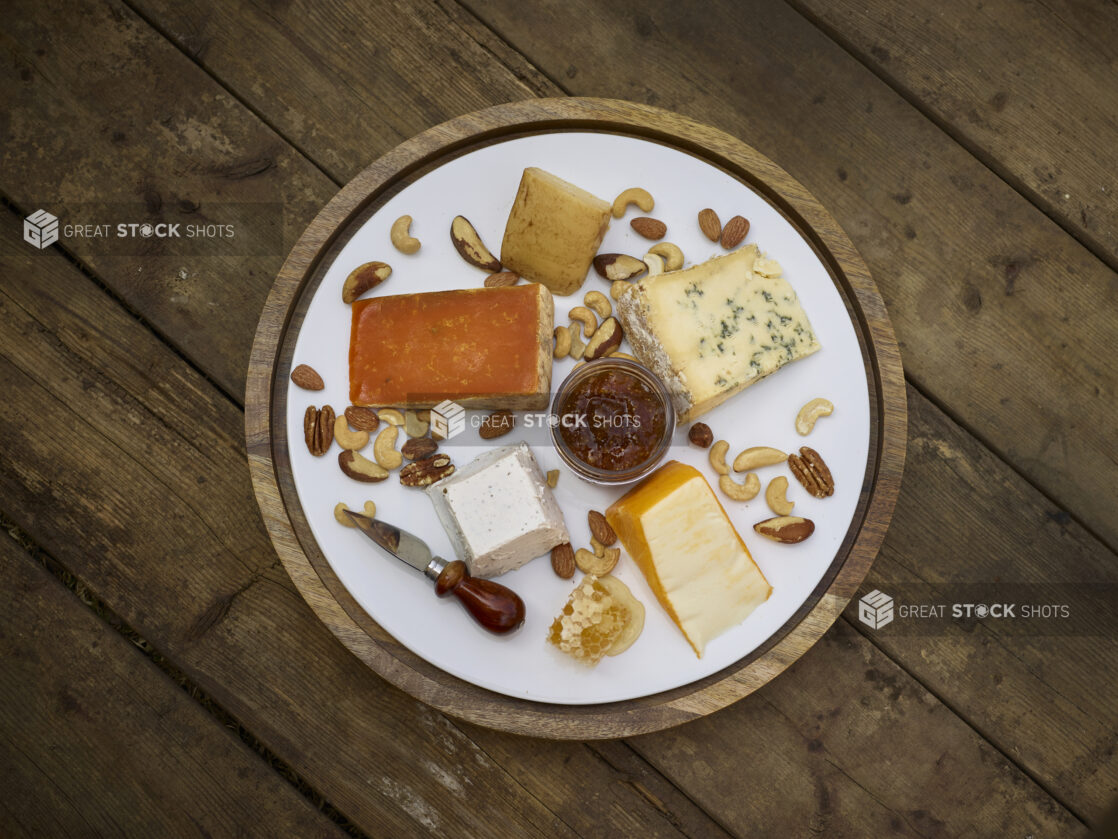 Cheese platter on a round wooden platter with various cheeses, nuts and honeycomb on a rustic wooden background